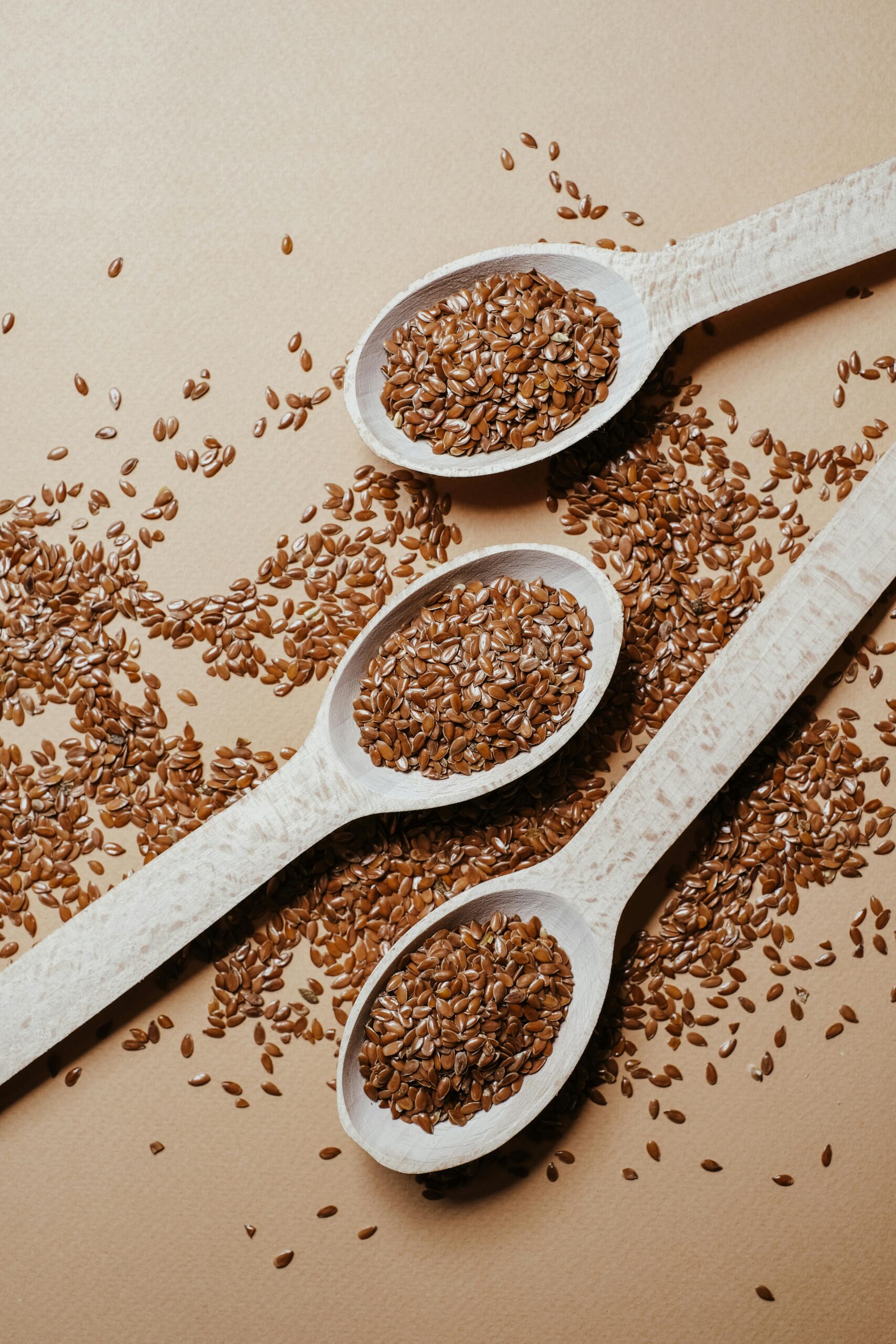 Three wooden spoons with flax seeds on a textured surface highlighting natural health food.
